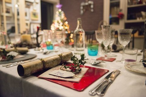 Miza, postavljena za božični obrok, s srebrnimi in kristalnimi kozarci in božično drevo v ozadju.