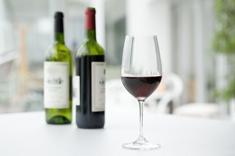 Rdeče vino v kozarcu in steklenice na mizi