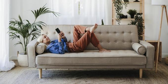 mlada ženska uporablja mobilni telefon, ki leži na kavču doma