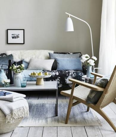 dnevna soba z blazinami na modrem vzorčastem kavču, bela talna svetilka, ki je nagnjena nad kavč, okraski, pike in vzorci krožnikov za impresionistični videz, sodoben in sproščen