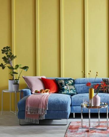 svetla dnevna soba z rumeno opaženo steno in modrim kavčem