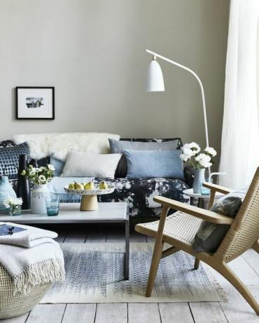 nevtralna dnevna soba, dnevna soba z blazinami na modrem vzorčastem kavču, upognjena bela talna svetilka nad kavčem kaplje, lise in vzorci krožnikov za impresionističen videz, ki je sodoben in sproščeno