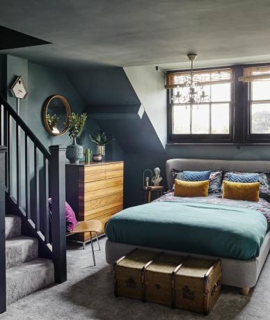 temno modra siva mansardna spalnica z lestencem in oblazinjeno posteljo